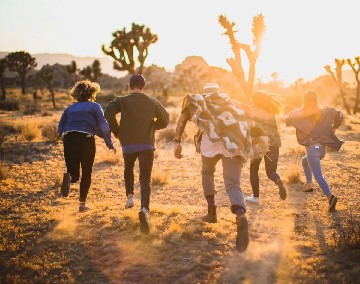 Five friends running together across open ground at sunset