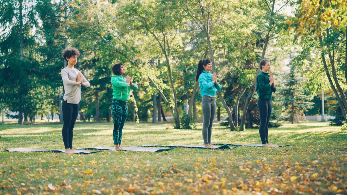 Four friends doing yoga together on mats in a park