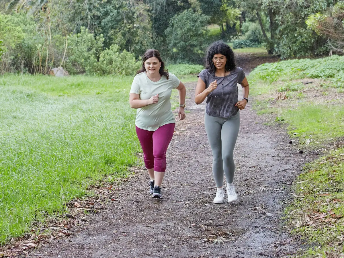 Two friends running side by side along a park trail