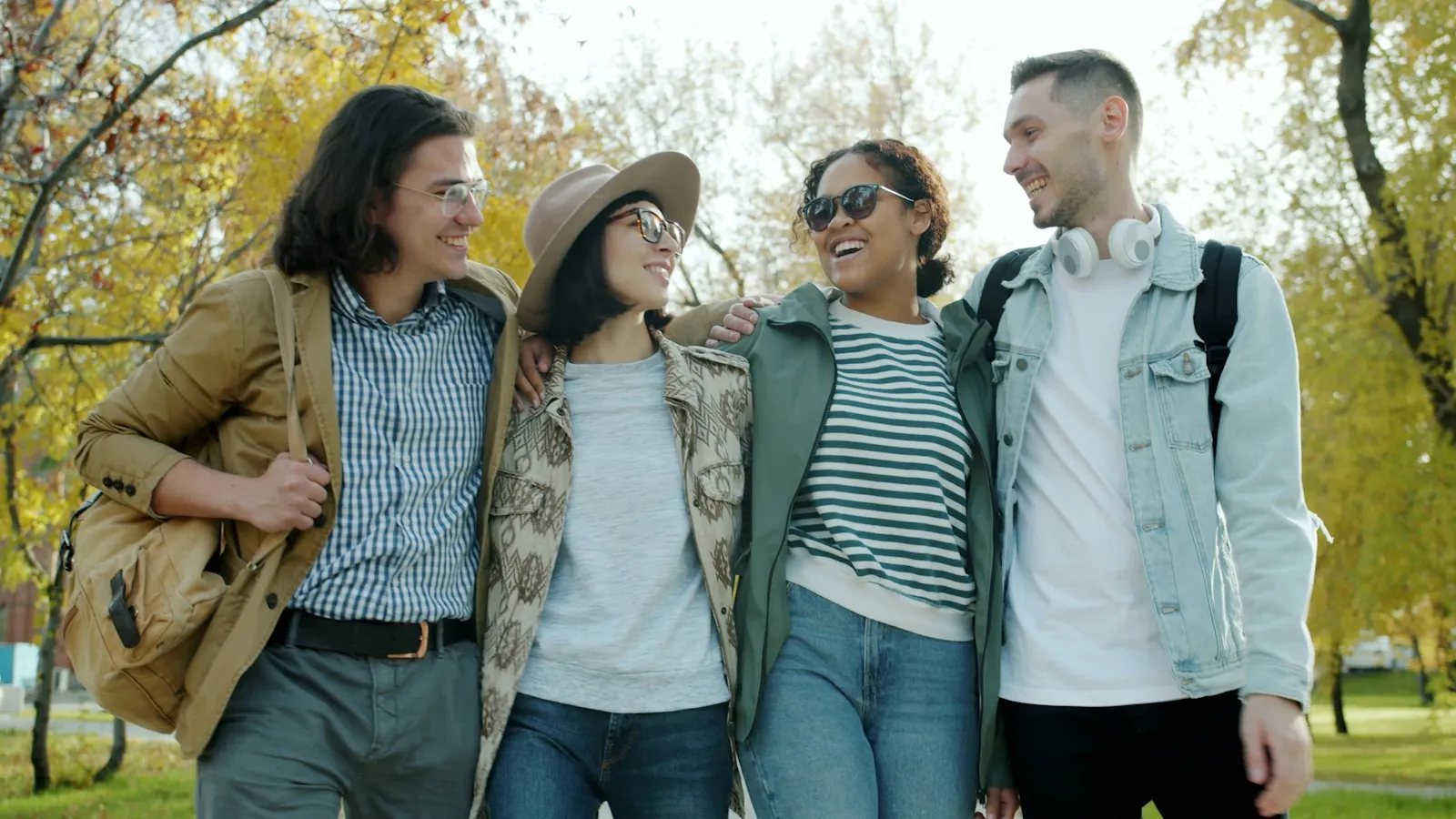 Four friends walking arm in arm through a sunny park, laughing together