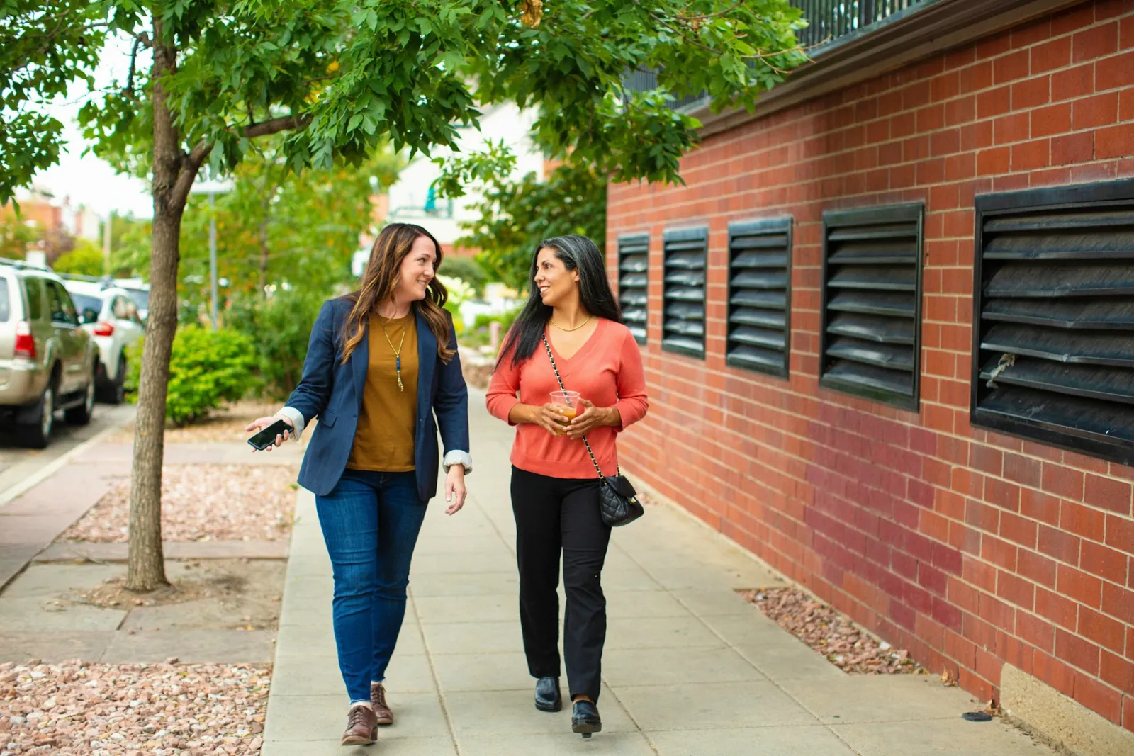 Two coworkers walking and chatting along a tree-lined sidewalk during the workday